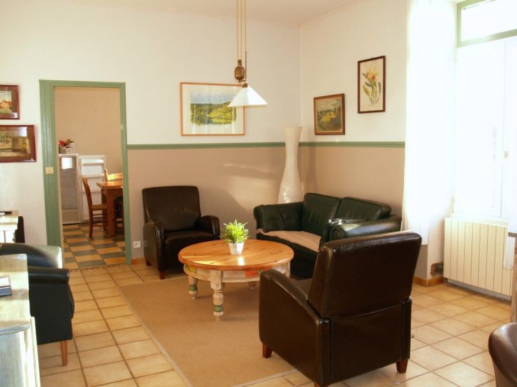 De woonkamer met leren fauteuils, houtkachel en doorkijk naar de eetkeuken