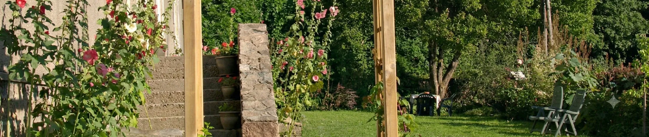 De tuin van L'Ancienne École met stokrozen, de stenen trap en het gazon in de ochtendzon
